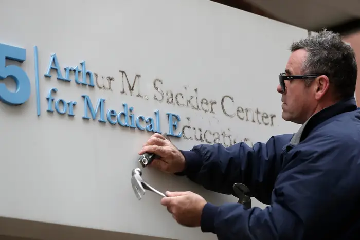Worker Gabe Ryan removes a sign that includes the name Arthur M. Sackler at an entrance to Tufts School of Medicine, in Boston, in late 2019. Tufts University said it is stripping the Sackler name from its campus in recognition of the family's connection to the opioid crisis